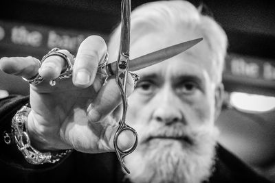 Close-up portrait of senior hipster barber holding scissors in salon