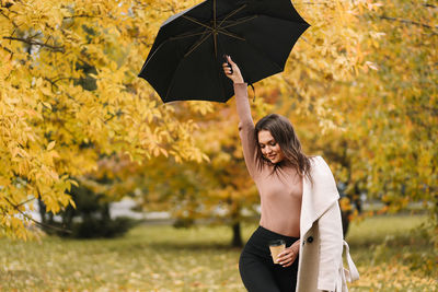 A beautiful cheerful girl walks under an umbrella in rainy weather in an autumn park in nature