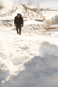 Rear view of man walking on snow covered land