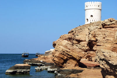 Lighthouse by sea against clear sky