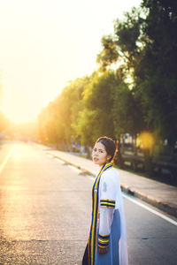 Portrait of woman standing on road against sky during sunset