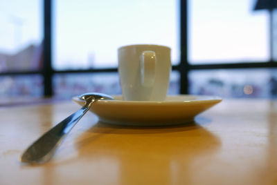 Close-up of coffee cup with spoon on table against glass window