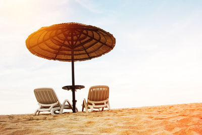 Empty chairs on beach against sky