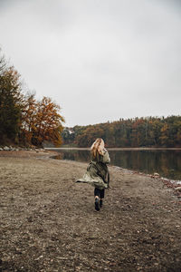 Rear view of woman wearing hat walking by lake against sky