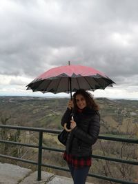 Portrait of smiling woman with umbrella standing on footpath by railing