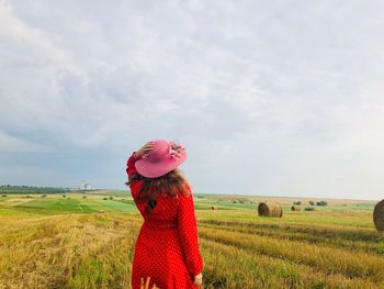 Back of woman wearing a red dress and a summer hat in the middle of a harvested field