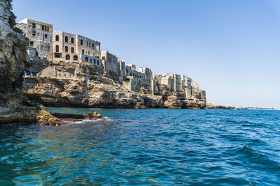 Sea by rocks against clear sky