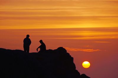 Silhouette people standing against orange sky during sunset