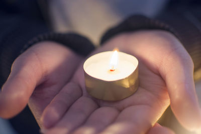 Close-up of hands with lit tea light candle