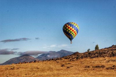 Colorful hot air balloon flying over field against sky