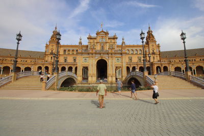 People at historical building against cloudy sky