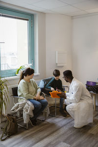 Male doctor talking to boy while crouching in waiting room at clinic