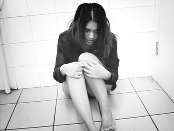 Beautiful young woman sitting on tiled floor at home