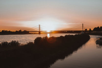 Silhouette bridge over river against sky during sunset