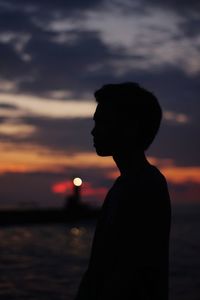 Side view of silhouette man standing at beach against sky during sunset