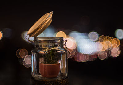 Close-up of houseplant in jar on table against illuminated light at night