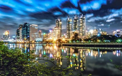 Illuminated buildings by river against sky at night