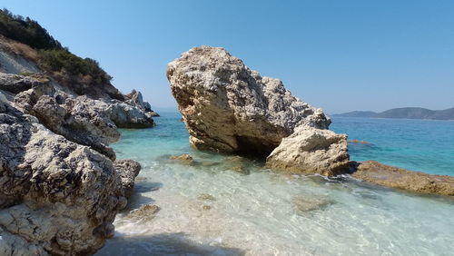 Rock formations in sea against clear blue sky