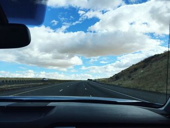 Car moving on country road against cloudy sky