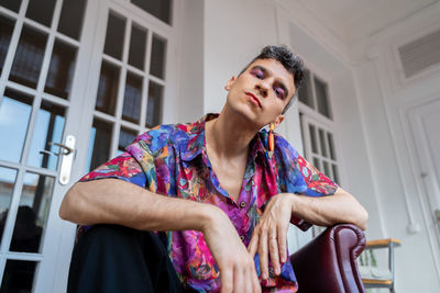 Portrait of confident transgender man in casual sitting on sideboard at home