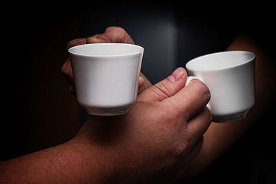 Close-up of hand holding coffee cup against black background