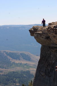 Distant view of man standing on cliff against clear sky