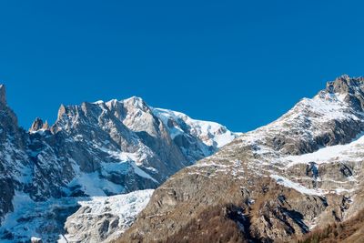 Low angle view of snowcapped mountains against clear blue sky