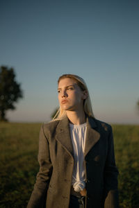 Young woman looking away on field against clear sky