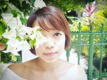 Close-up portrait of young woman standing by white flowers blooming outdoors