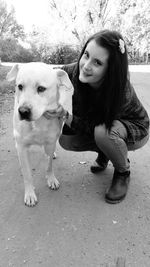 Portrait of young woman embracing dog while crouching on dirt road