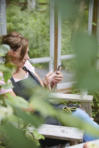 Female gardener using mobile phone while sitting in yard