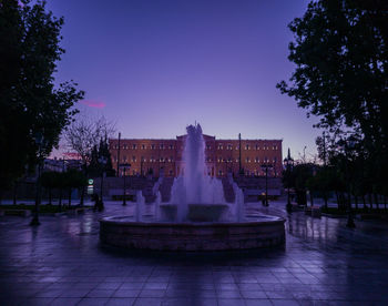 Fountain in city against clear sky at dusk