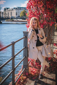 Portrait of young woman using phone while leaning on railing by creeper plant