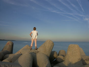 Girl with white shirt standing on concrete jetty piling facing the sea after sunset