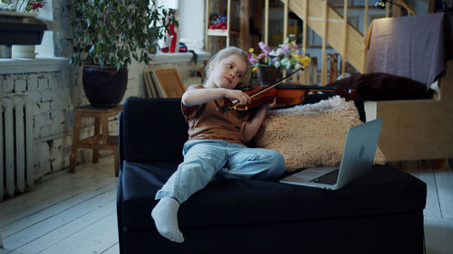 Girl playing violin on sofa at home