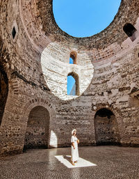 Woman standing inside ancient roman building with natural light shining on her.