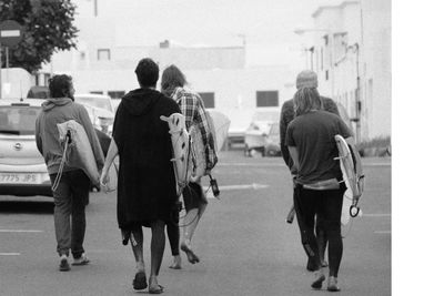 Rear view of men walking with surfboards