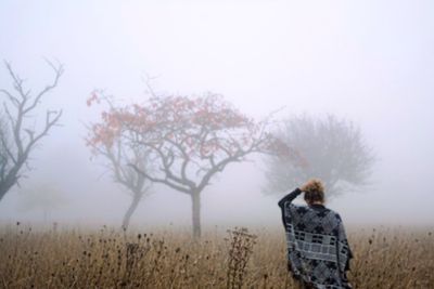Rear view of woman standing amidst field during foggy weather