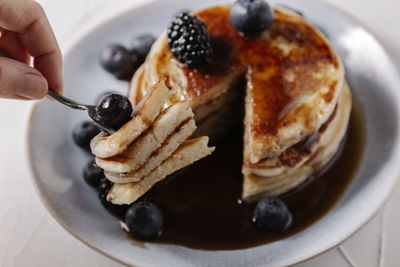 Woman sticking pancakes with a blueberry on a fork