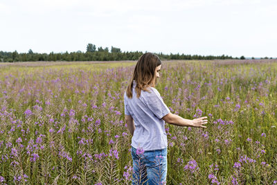 Young beautiful smiling blond woman  walking in meadow among flowers of fireweed and touching flower