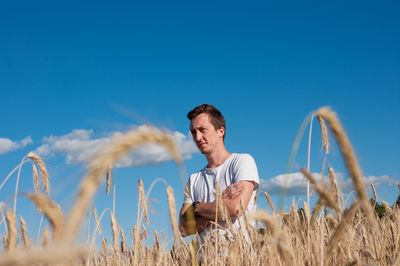 Thoughtful man standing amidst wheat plants against sky