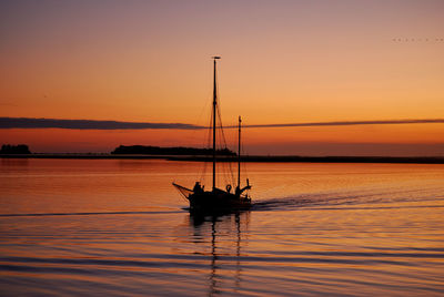 Silhouette sailboat in sea against sky during sunset