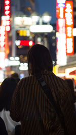 Rear view of woman standing on illuminated street at night