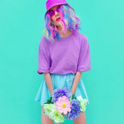 Portrait of woman holding flowers standing against colored backgrounds