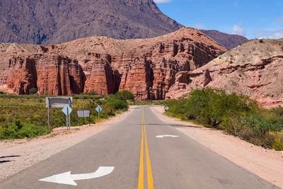 Road leading towards rocky mountains against sky