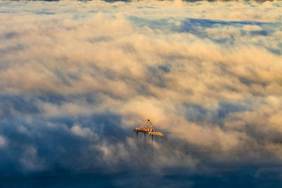 Shipping crane peeking out of clouds at sunset