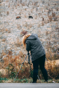 Rear view of woman photographing horses through camera