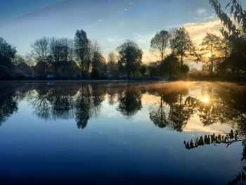 Reflection of trees in lake against sky at sunset