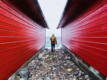 Rear view of young man walking on walkway by houses against sea