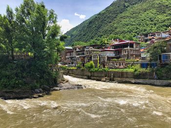 River amidst houses and trees against sky